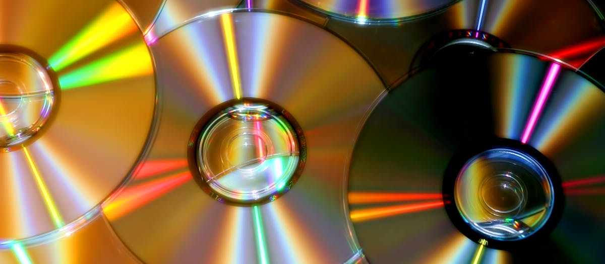 A close-up photo of compact discs reflecting colorful light patterns.