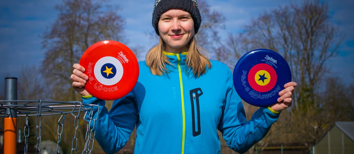 Young woman holding frisbee golf discs, enjoying a sunny day in an Estonian park.